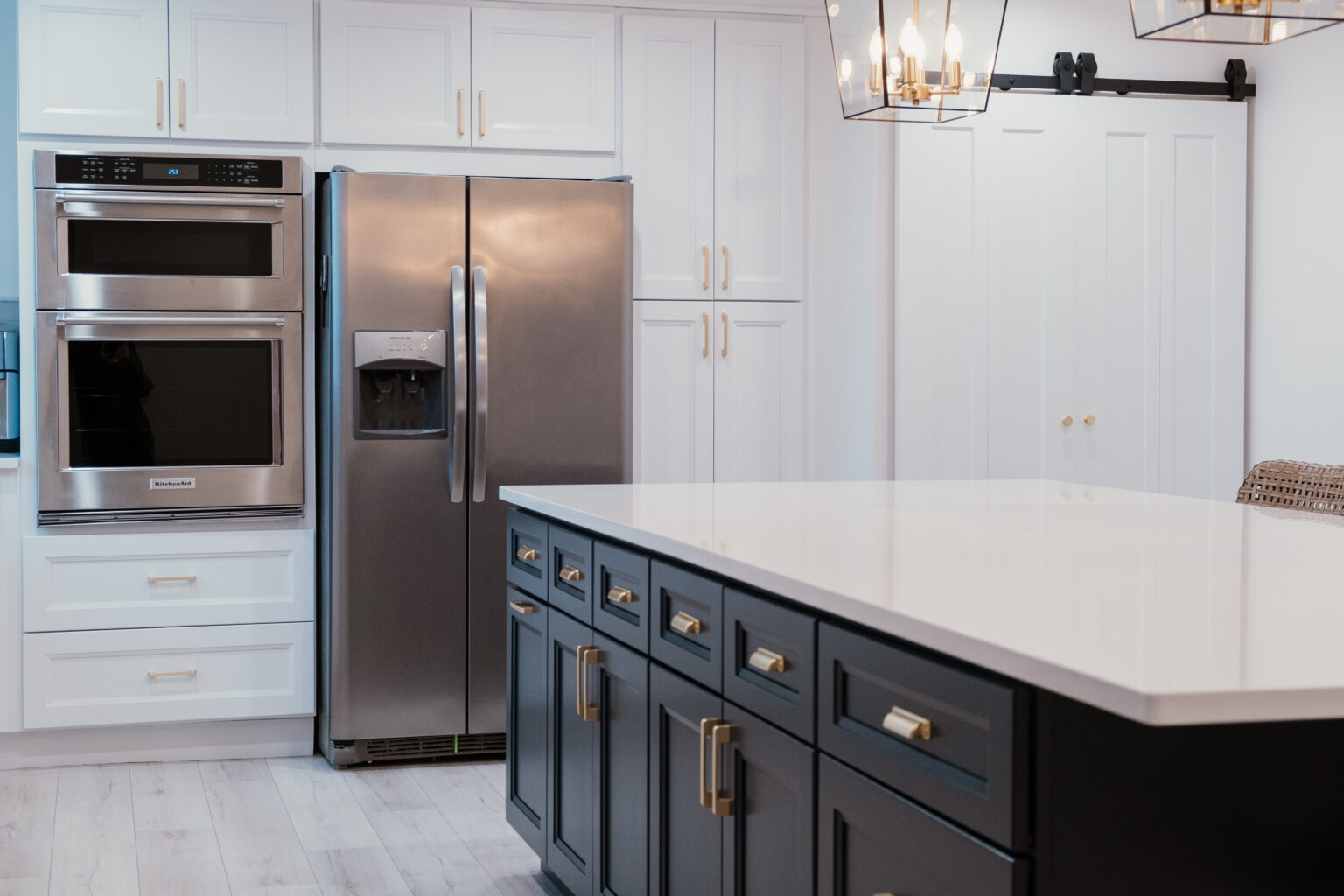 Kitchen with white appliance-wall cabinets, dark blue island, gold-tone pulls, and a sliding white door.