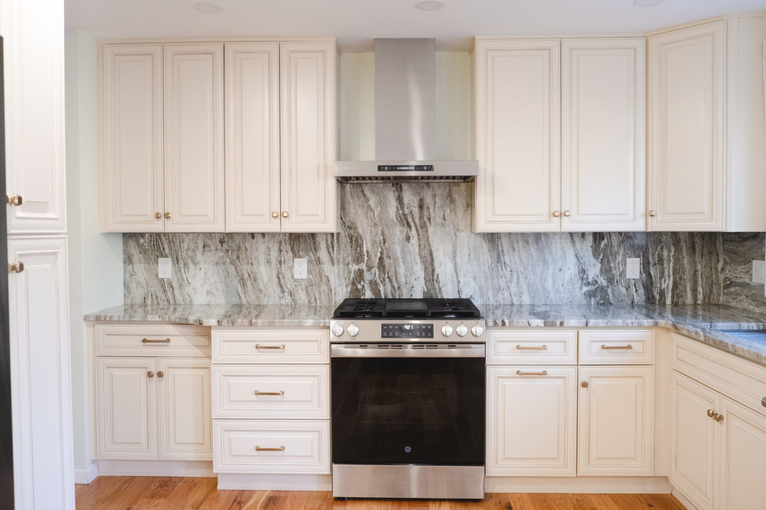 White detailed cabinets surrounding a centered range and full-height gray-and-white veined backsplash.