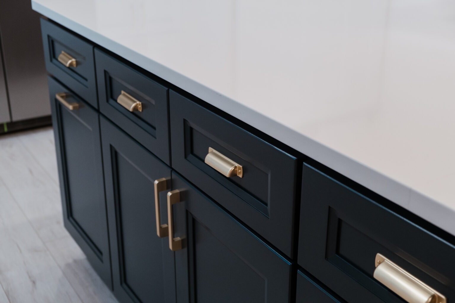Dark blue cabinets and drawers with gold-tone cup pulls and bar handles beneath a white countertop.