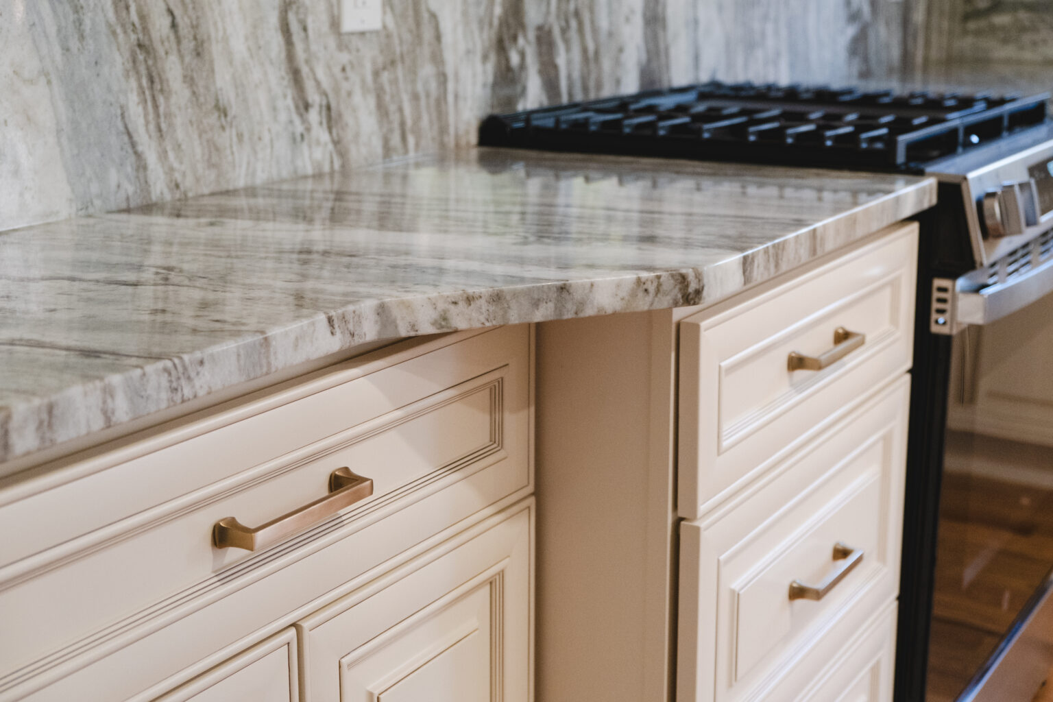 White detailed drawers with gold-tone pulls, a gray-and-white veined countertop, and range edge.
