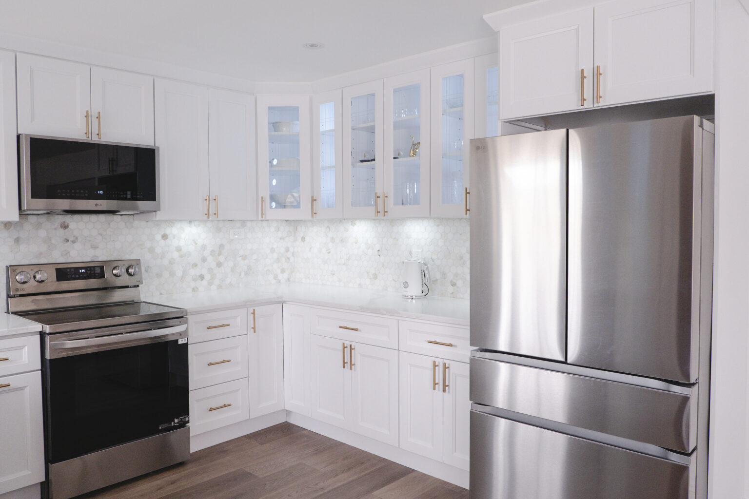 White kitchen cabinets with glass-front uppers, hexagonal backsplash, and large silver appliances.